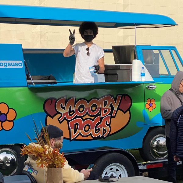 The food truck is a VW Bus Painted to look like the Mystery Machine from Scooby Doo. The chef waves happily from inside.