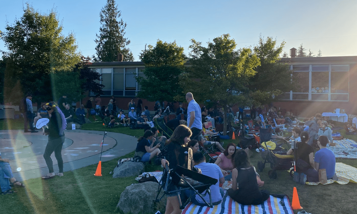 people in lawn chairs and on picnick blankets enjoy a lovely evening in the park.