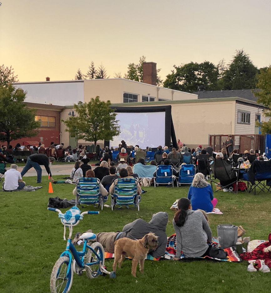 The crowd lounges on the lawn watching the movie.