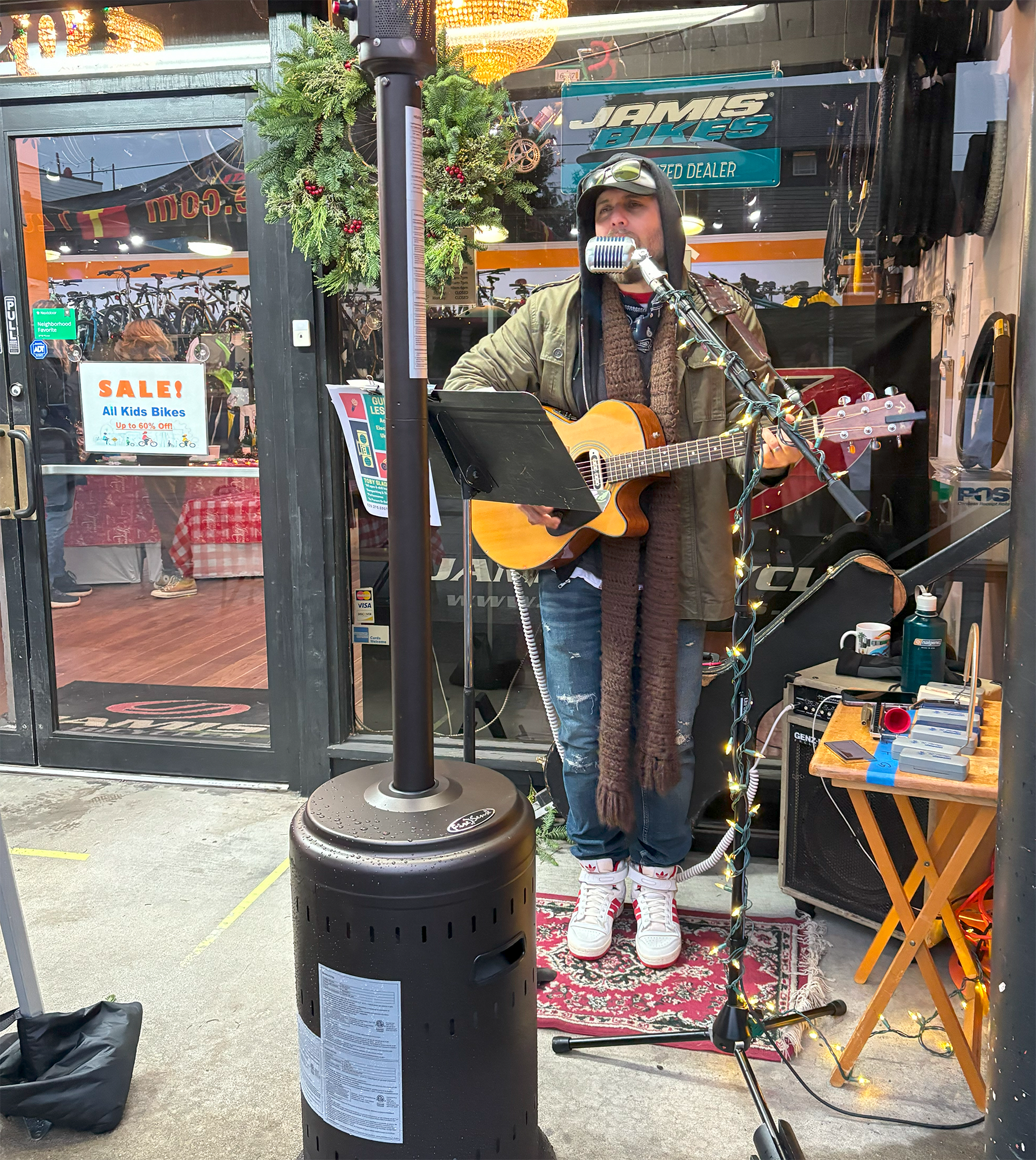 Musician plays guitar and sings in front of neighborhood business.