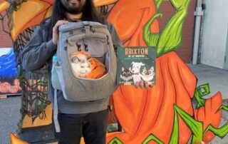 A man poses with his cat, costumed as a pumpkin