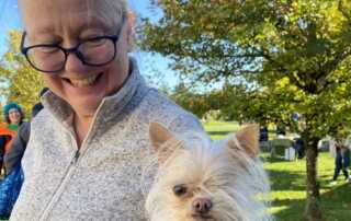 A volunteer smiles down at her small dog.